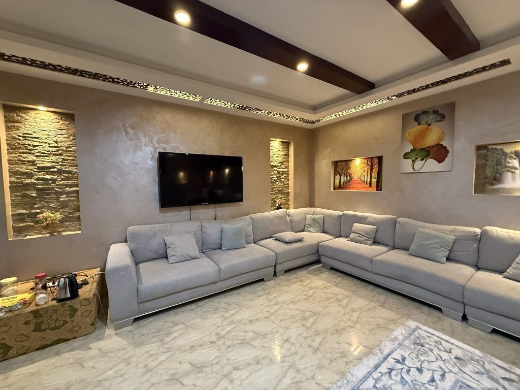 Una sala de estar moderna con un sofá modular, un televisor de pantalla plana, arte decorativo en la pared y suelo de mármol.