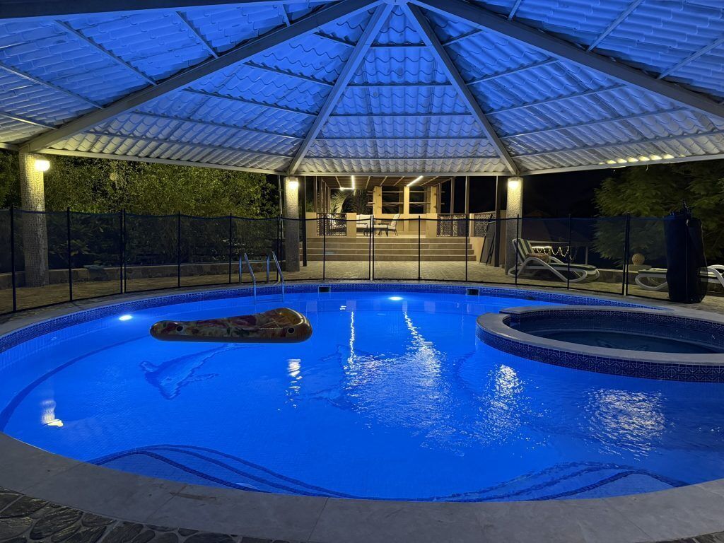 Una piscina interna con tetto in vetro, circondata da una recinzione, e un'area relax con sedie.