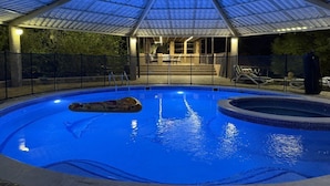 Piscina interna com teto de vidro, cercada por grade e área de estar com cadeiras.