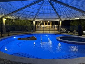 Ein Innenpool mit Glasdecke, umgeben von einer Umzäunung, und ein Sitzbereich mit Stühlen.