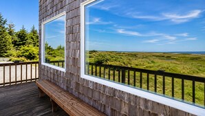 A wooden deck with a bench and large windows overlooking a natural landscape.