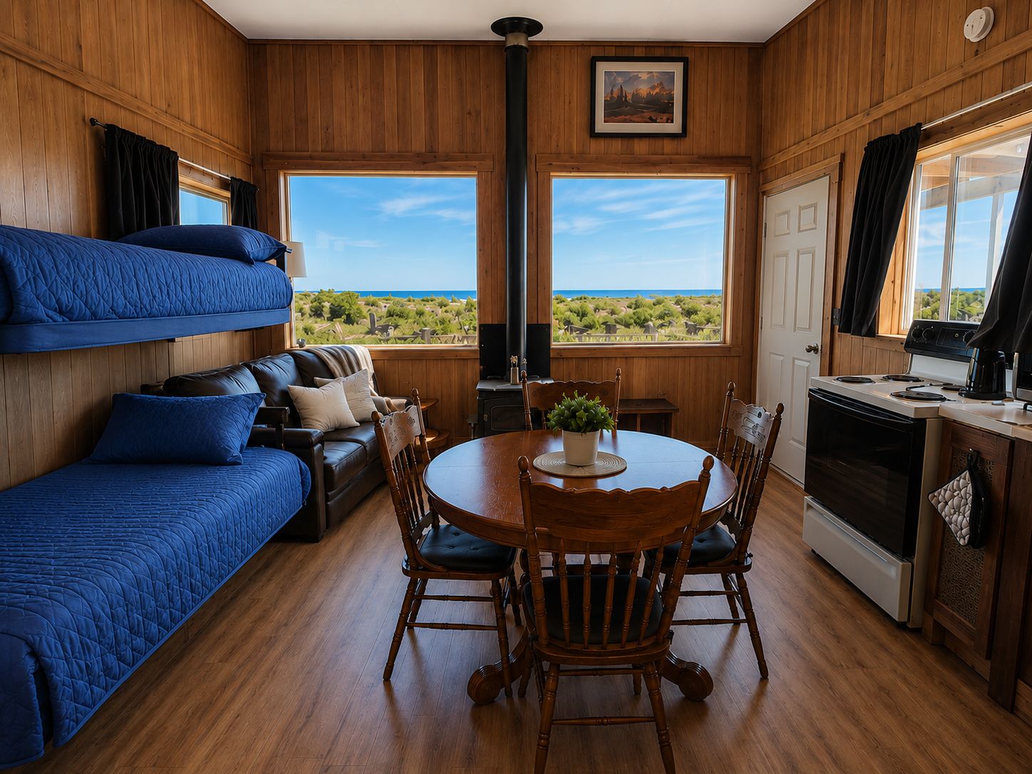 Ein Zimmer mit Etagenbetten, einem Esstisch mit Stühlen, einem Herd und Blick ins Freie.