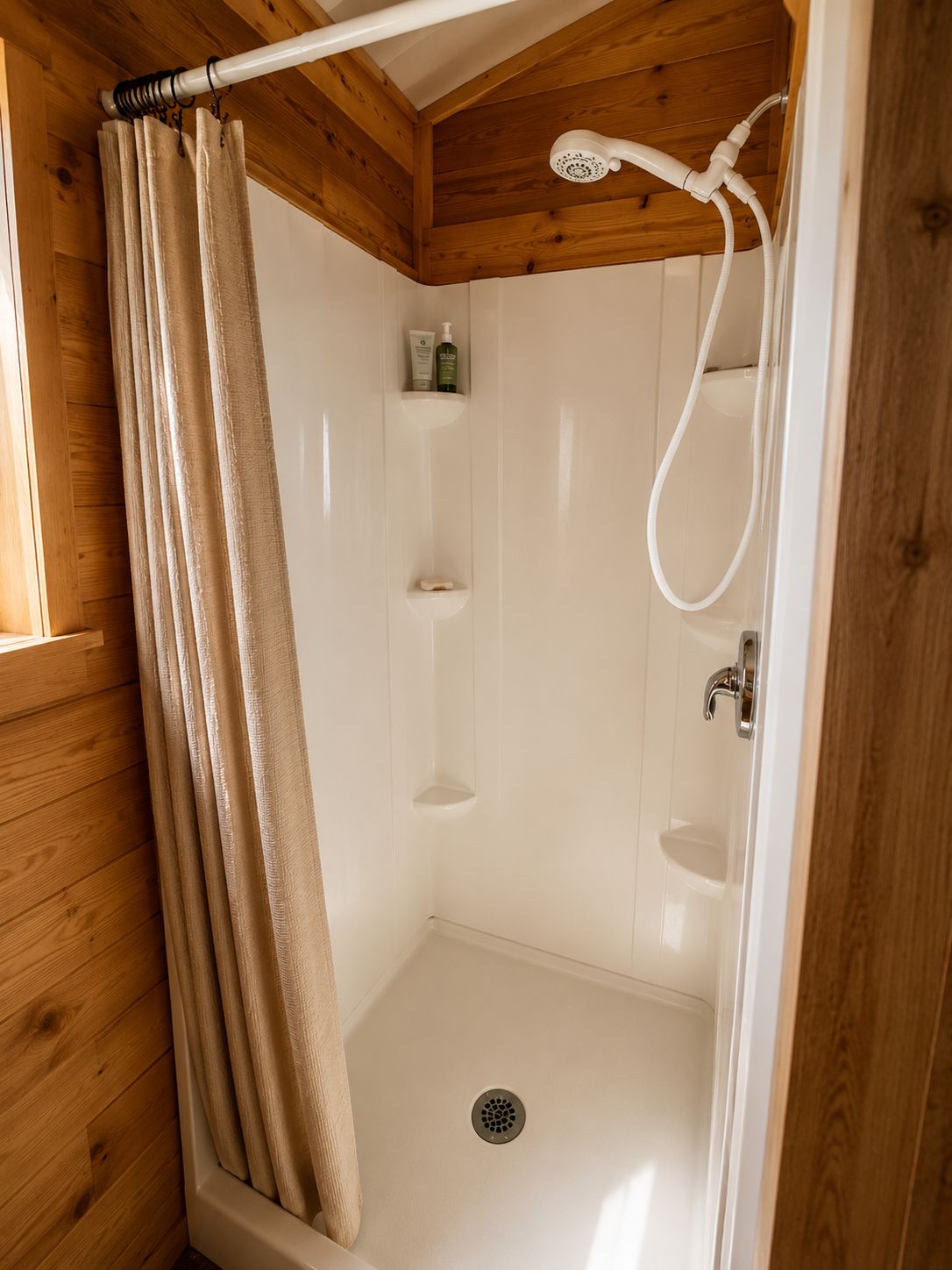 Area doccia con soffione, tenda e ripiano con articoli da toilette.