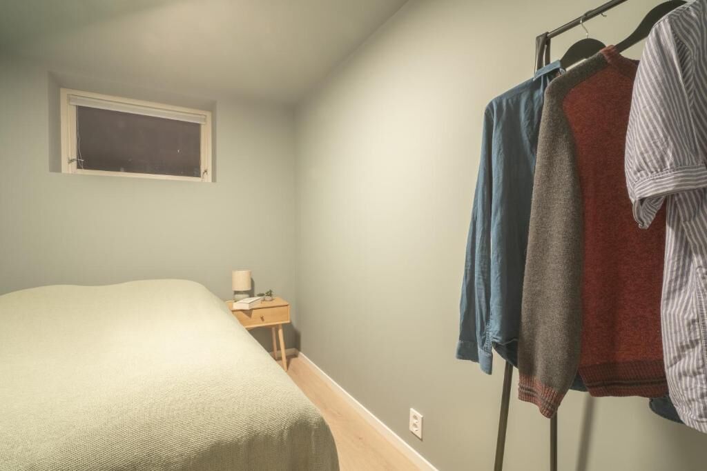 A bedroom with a bed, a nightstand, a window, and a clothing rack with several garments.