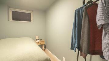 A bedroom with a bed, a nightstand, a window, and a clothing rack with several garments.