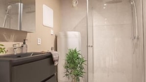 Um banheiro moderno com box de vidro, toucador escuro e um vaso de planta.