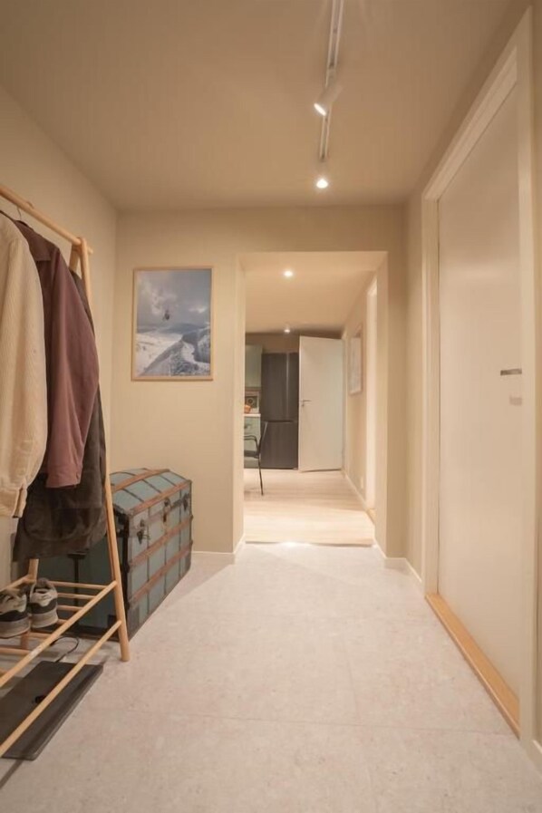 A hallway with a coat rack, a suitcase, and a framed picture on the wall.
