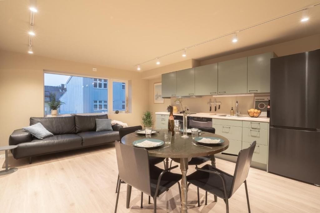 A modern kitchen with a dining area, a sofa, and a view of a building outside.