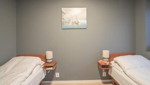 Quarto de hotel com duas camas, um quadro na parede e mesas de cabeceira com luminárias e livros.