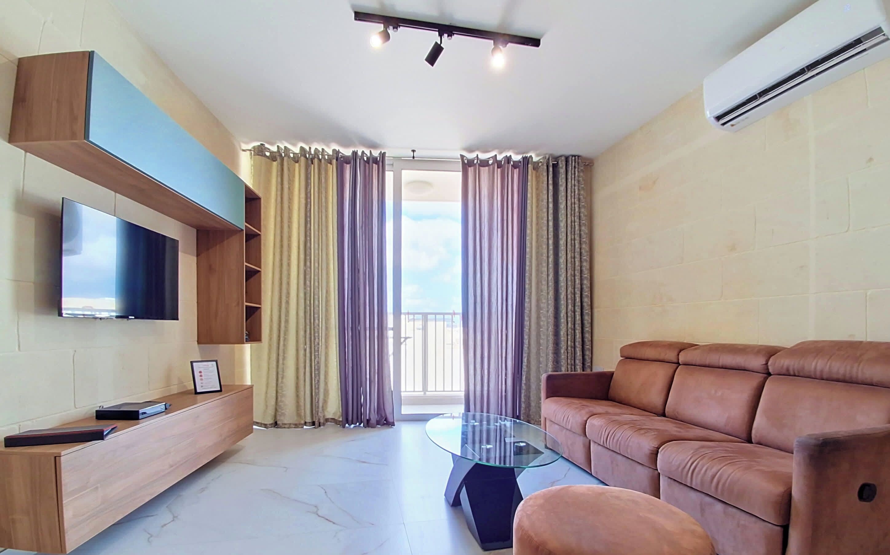 A modern living room with a flat-screen TV, a glass coffee table, a leather sofa, and a built-in TV shelf.