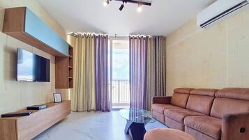 A modern living room with a flat-screen TV, a glass coffee table, a leather sofa, and a built-in TV shelf.