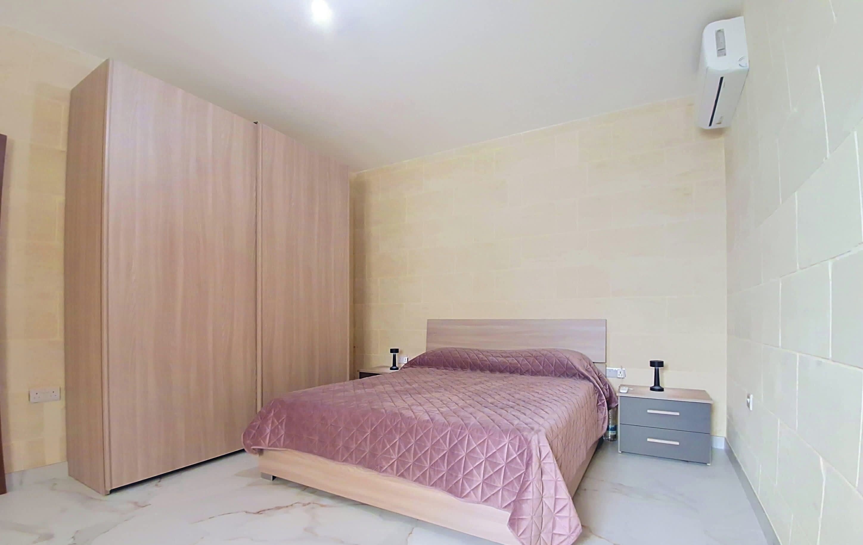 Un dormitorio con cama, armario, mesita de noche y aire acondicionado.