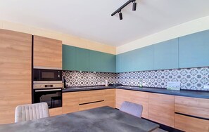 A modern kitchen with wooden cabinets, a microwave, and a patterned backsplash. - Spacious 2BR Family Apt in Central Gozo Location (Ix-Xewkija)
