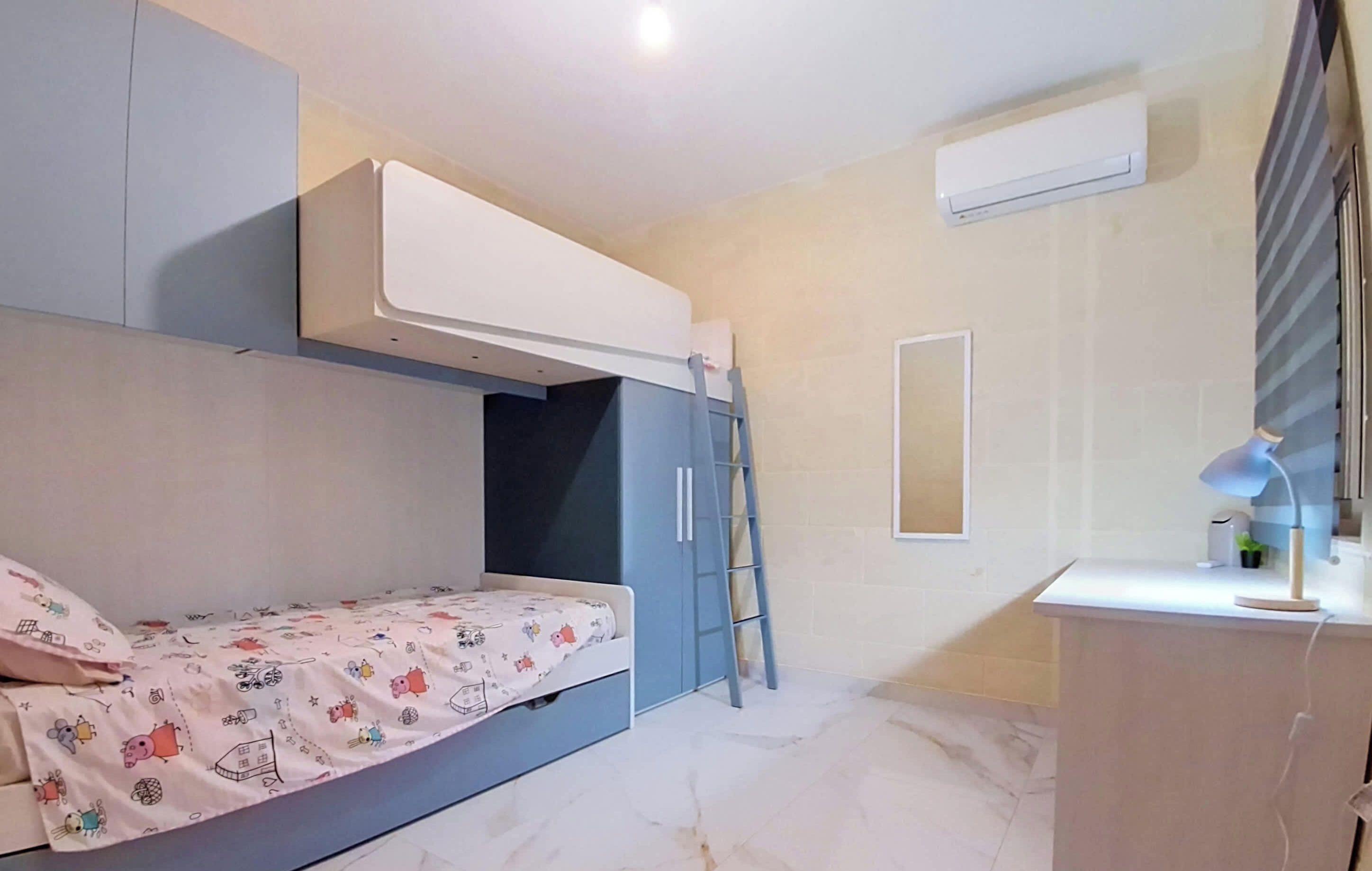 Ein Schlafzimmer mit Etagenbett, Schreibtisch und einer Lampe sowie einer Klimaanlage.