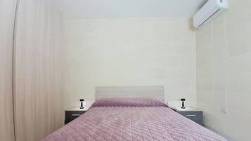 A bedroom with a bed, nightstands, an air conditioning unit, and a curtain.