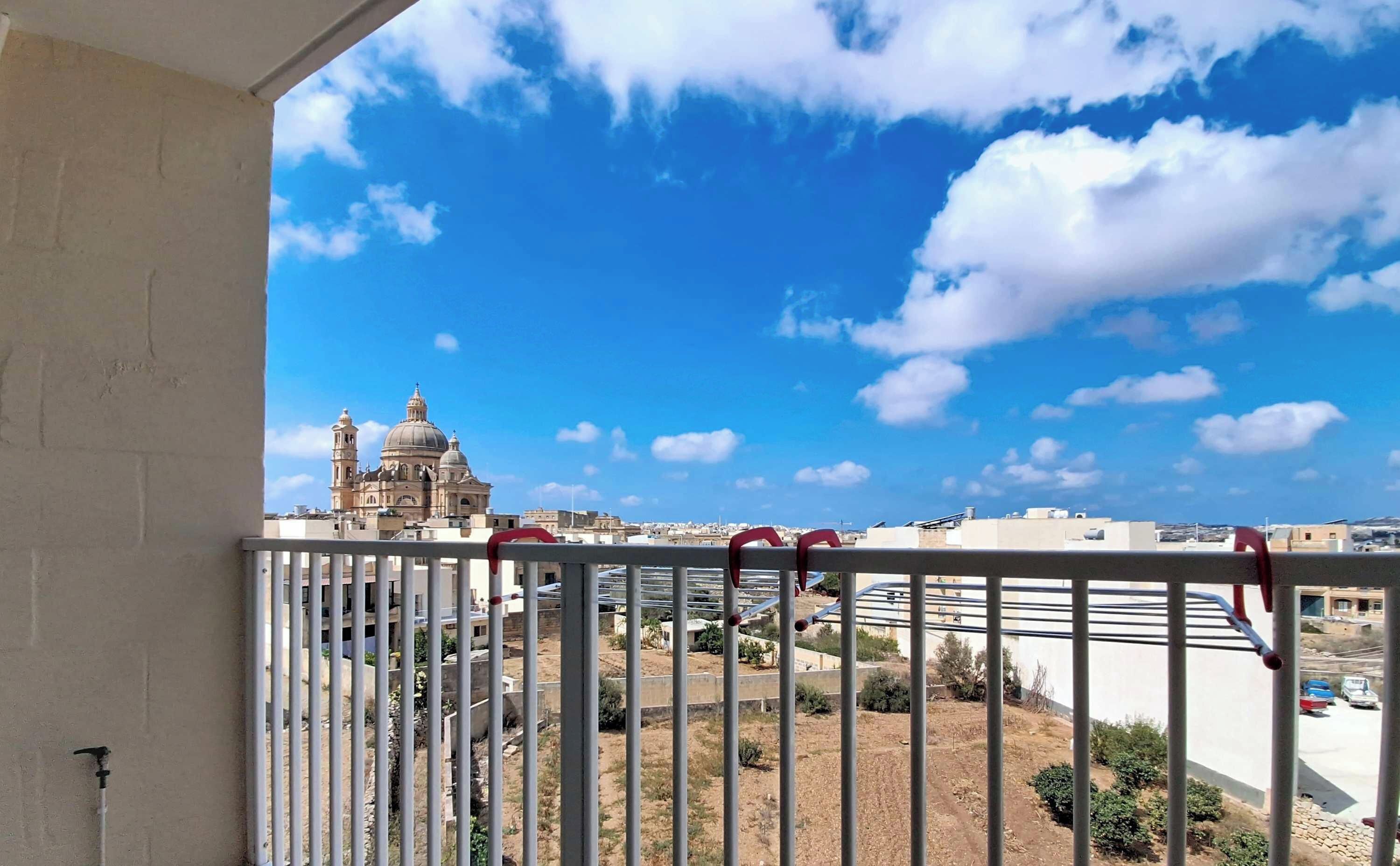 Un balcón con barandilla de metal que ofrece vistas a un paisaje urbano, incluyendo una iglesia destacada con cúpulas y torres.