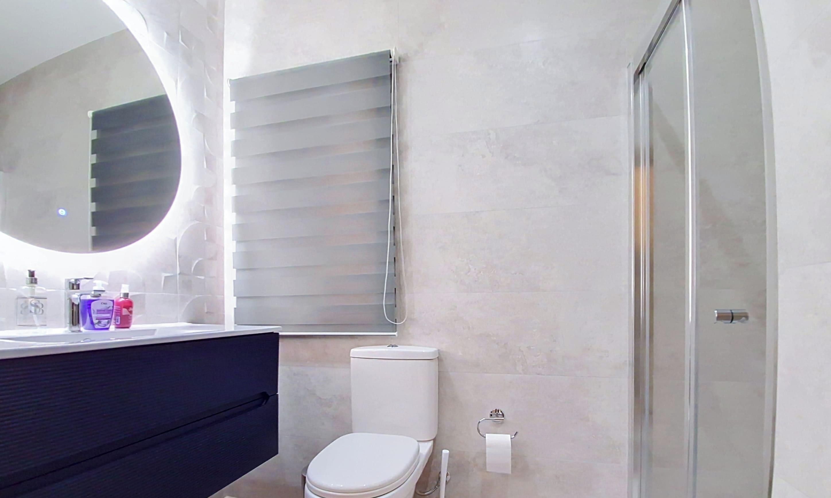 Un bany modern amb vàter, un lavabo amb articles de tocador, un mirall i una dutxa.