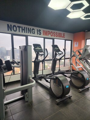 Ein Fitnessstudio mit Laufbändern und Trainingsgeräten, großen Fenstern mit Blick auf die Stadt und einem motivierenden Schild mit der Aufschrift 'NOTHING IS IMPOSSIBLE'.