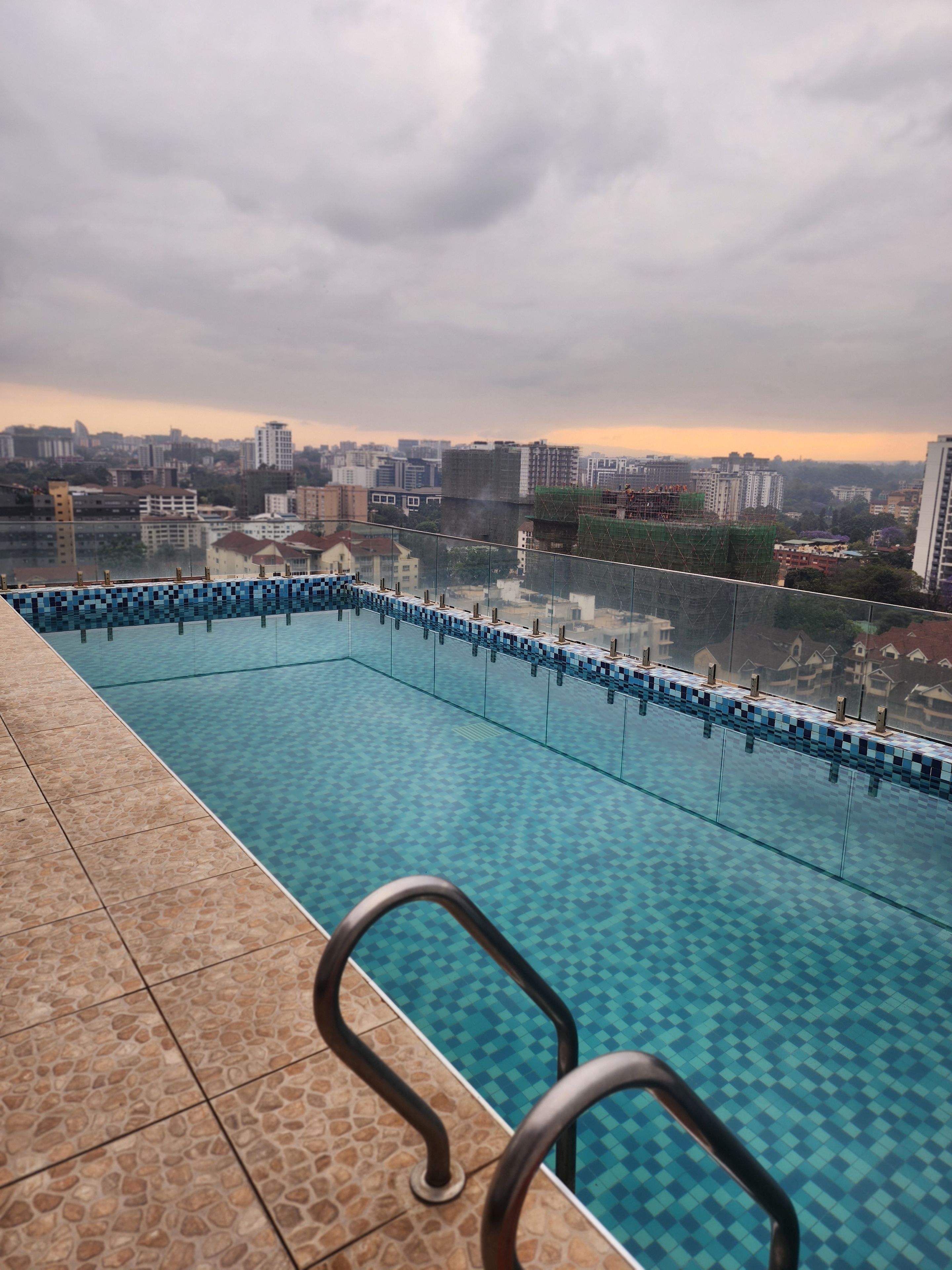 A swimming pool with a tiled edge and a metal handrail, surrounded by a tiled deck.