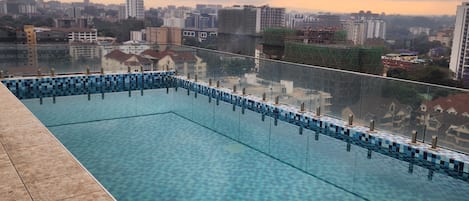 A swimming pool with a tiled edge and a metal handrail, surrounded by a tiled deck.