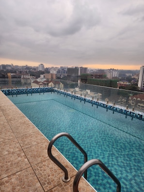 Ein Schwimmbecken mit einer gefliesten Kante und einem Metallgeländer, umgeben von einer gefliesten Terrasse.