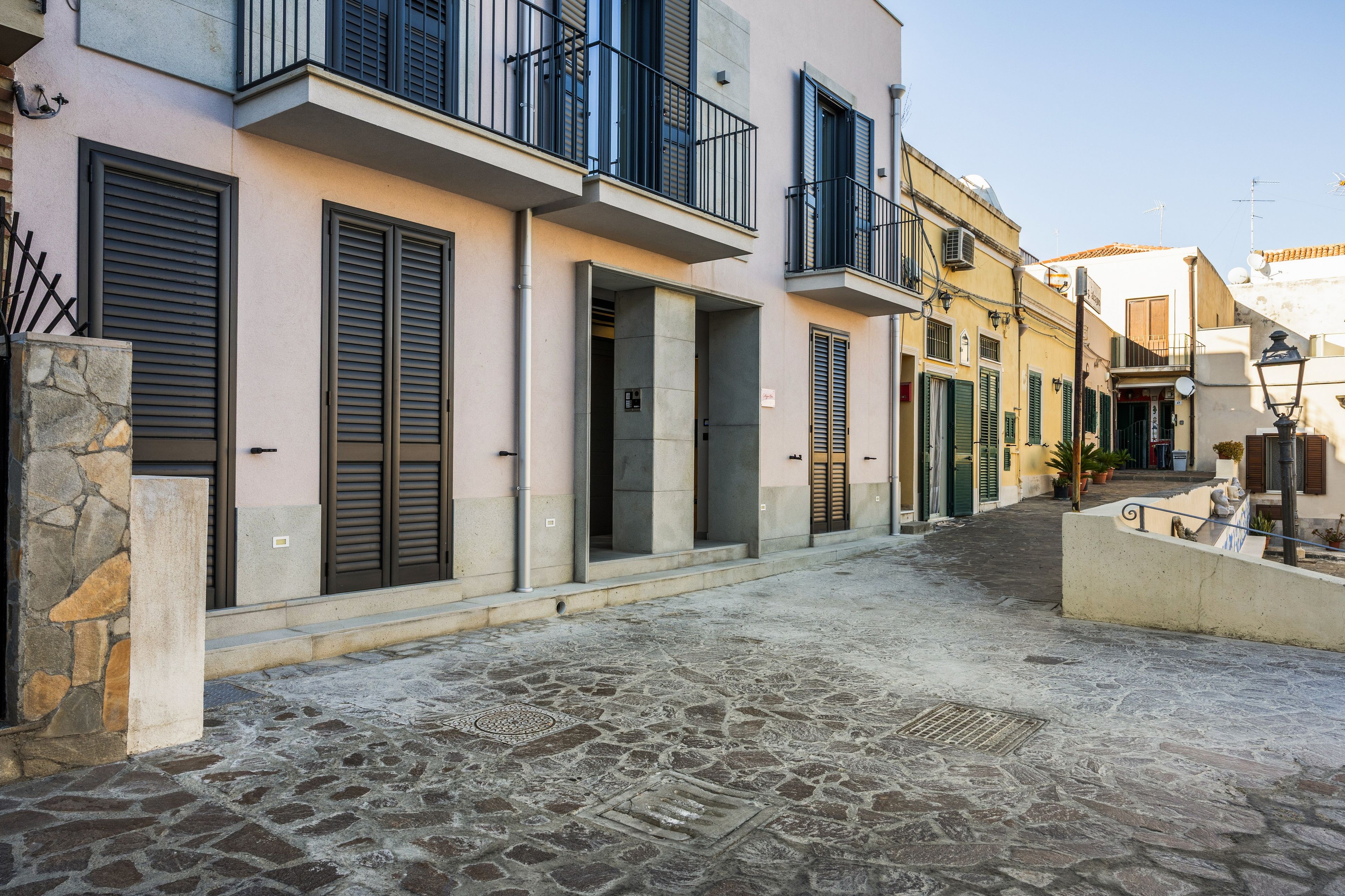 Une ruelle étroite pavée, bordée d’immeubles dotés de balcons et de volets.