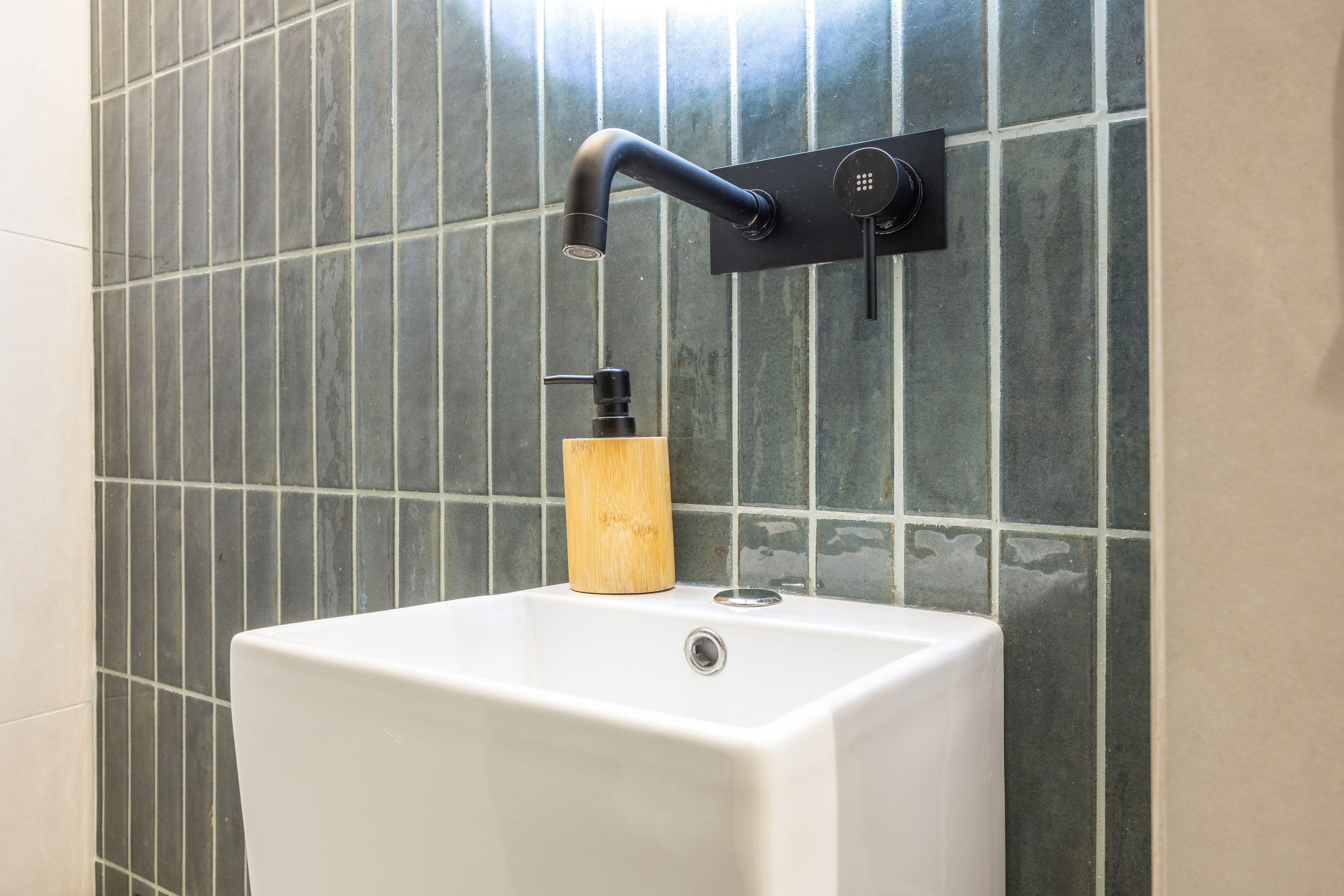A bathroom with a white pedestal sink, a black faucet, and a wooden soap dispenser.