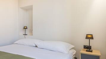 Quarto simples com uma cama, mesa de cabeceira e luminária.