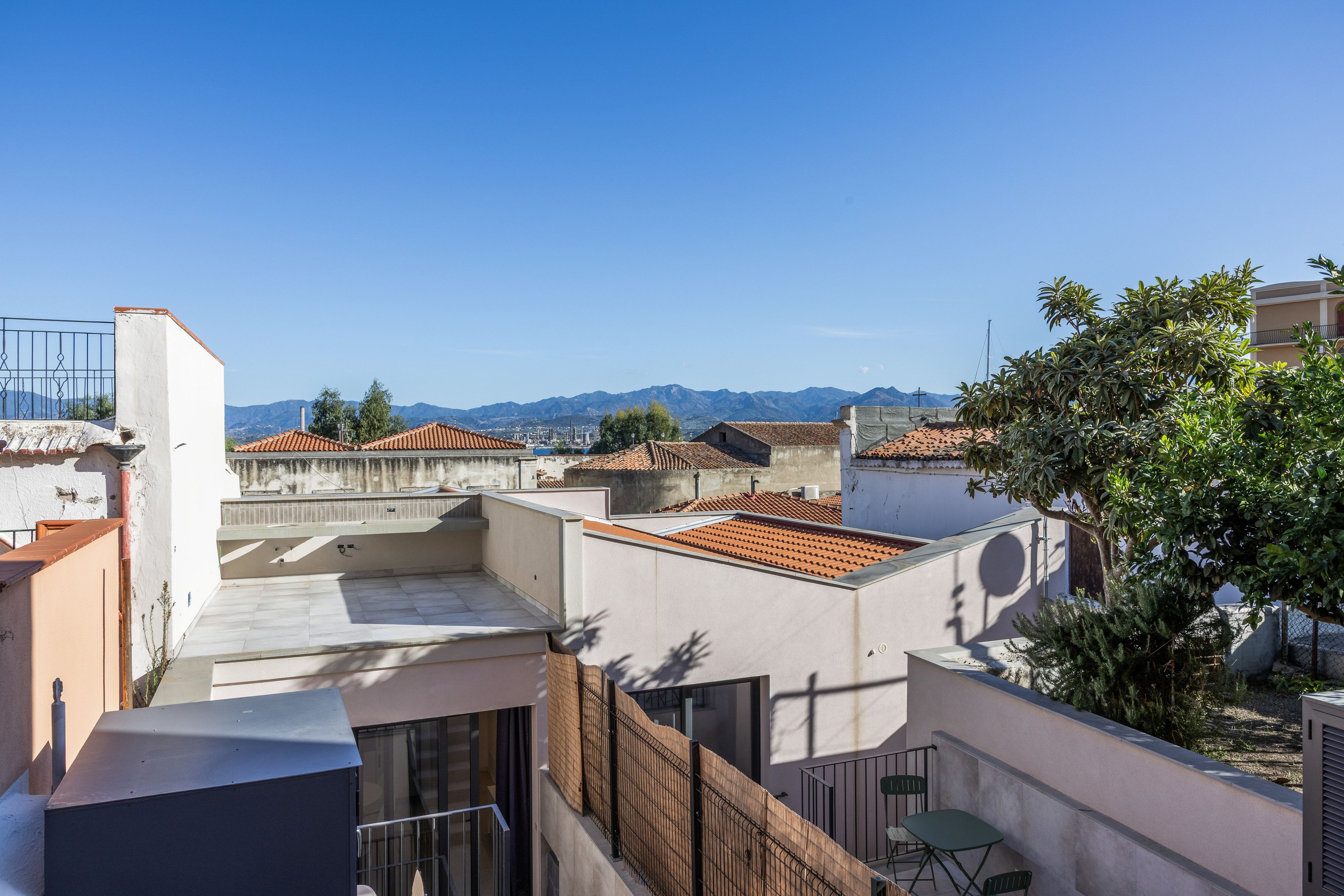 Una terraza en la azotea con vistas a montañas distantes, una pequeña mesa y sillas, y un árbol.