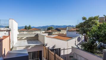 Una terraza en la azotea con vistas a montañas distantes, una pequeña mesa y sillas, y un árbol.