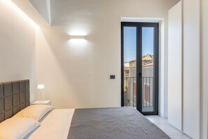 A bedroom with a bed, a nightstand, a lamp, and a view of the outside through a door. - Calcagno Home vacation house with private terrace, Wi-Fi, and air conditioning (Milazzo)