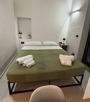 Uma cama de solteiro com colchão verde, almofadas brancas e duas toalhas enroladas.