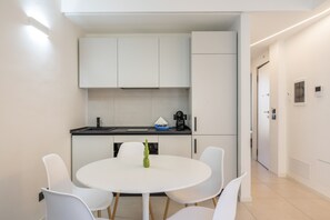 A modern kitchen with white cabinets, a round dining table with four chairs, and a coffee machine. - Calcagno Home vacation house with private terrace, Wi-Fi, and air conditioning (Milazzo)