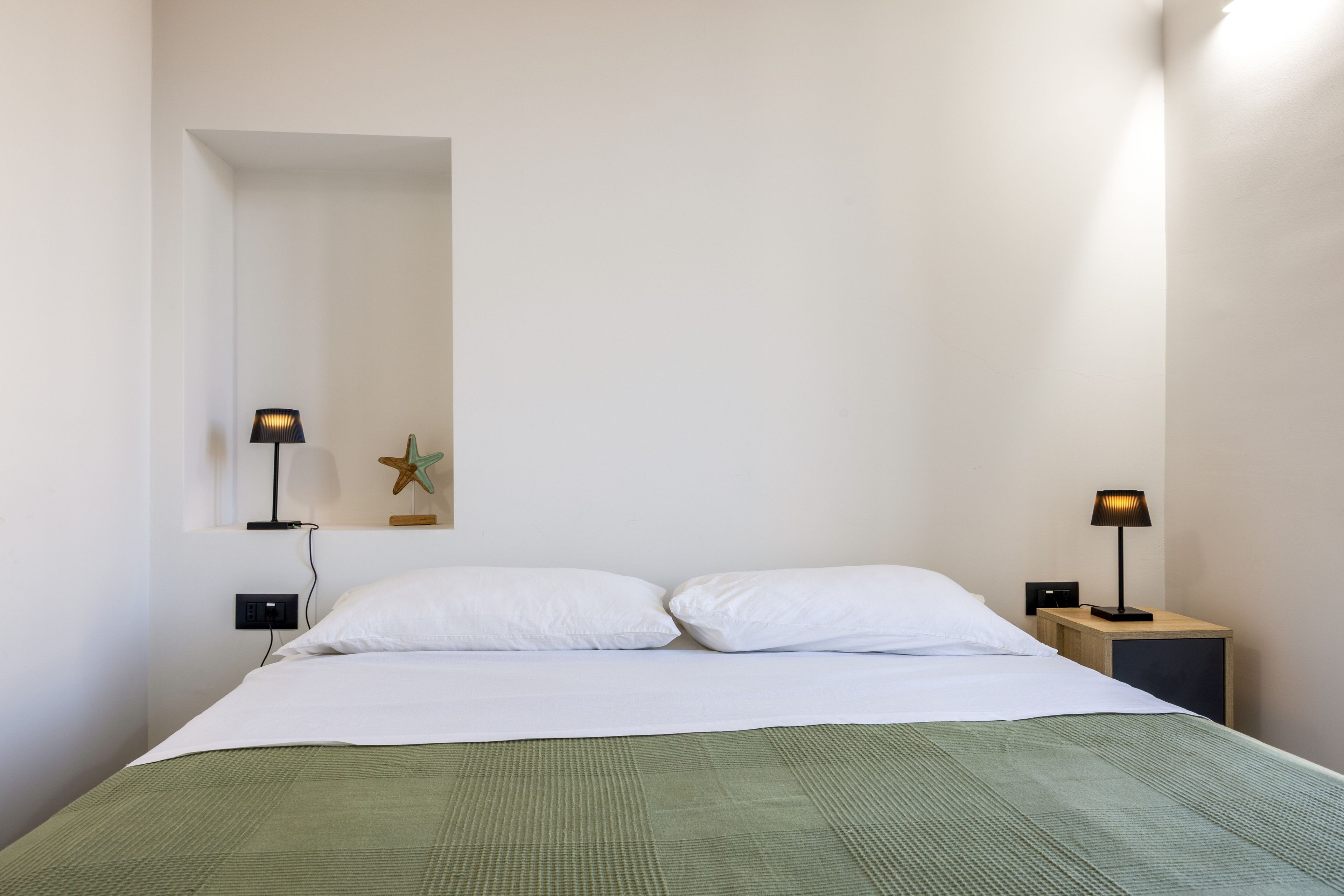 A bedroom with a bed, two bedside tables, two lamps, a starfish decoration, and a power outlet.