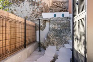 Um corredor exterior estreito, com parede de pedra, portão de metal e um degrau que leva a uma porta com puxador de metal.