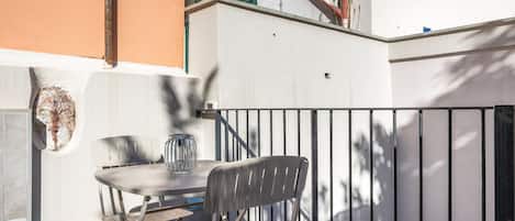 An outdoor seating area with a table and chairs, a metal railing, and a building facade in the background.