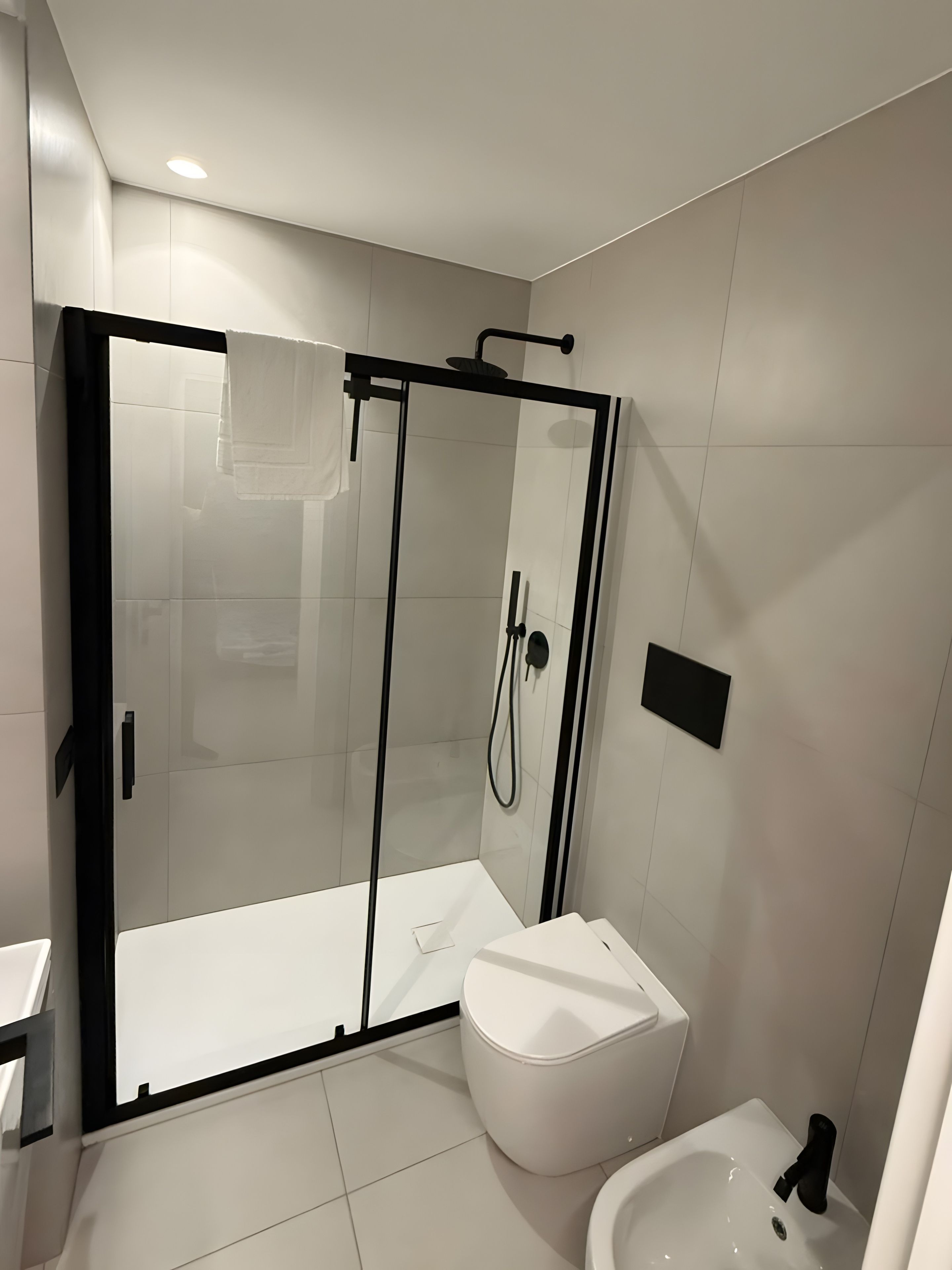 A modern bathroom with a glass-enclosed shower, a white toilet, and a bidet.
