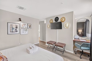 Ein modernes Hotelzimmer mit einem großen Bett, einem flachbildfernseher an der Wand, einem Schreibtisch mit Stuhl und einem Spiegel.