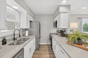 Une cuisine moderne dotée d’appareils électroménagers en acier inoxydable, de meubles blancs et d’un plancher en bois.
