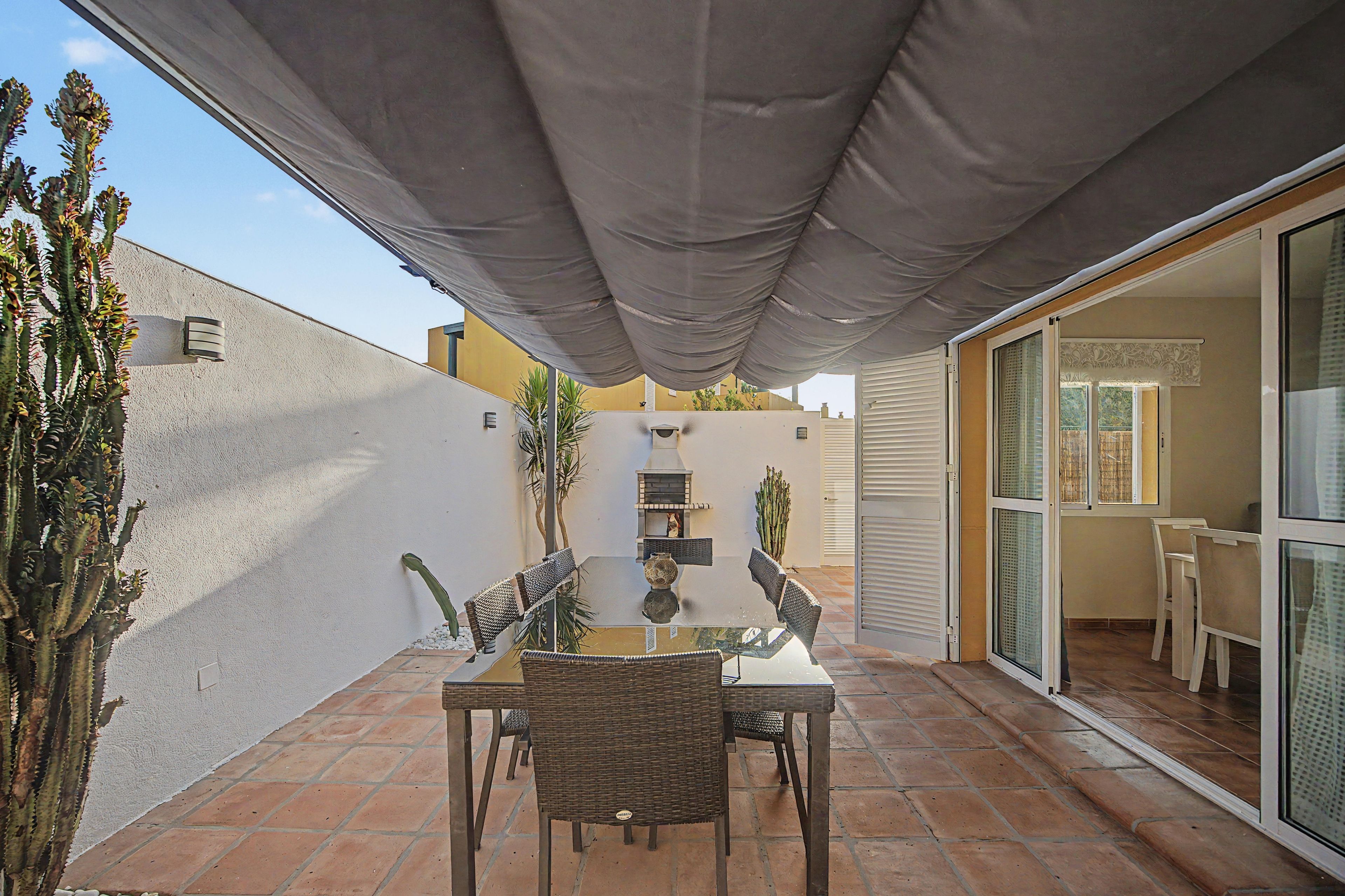 An outdoor patio with a table and chairs, a pergola providing shade, and a view of the adjacent building.