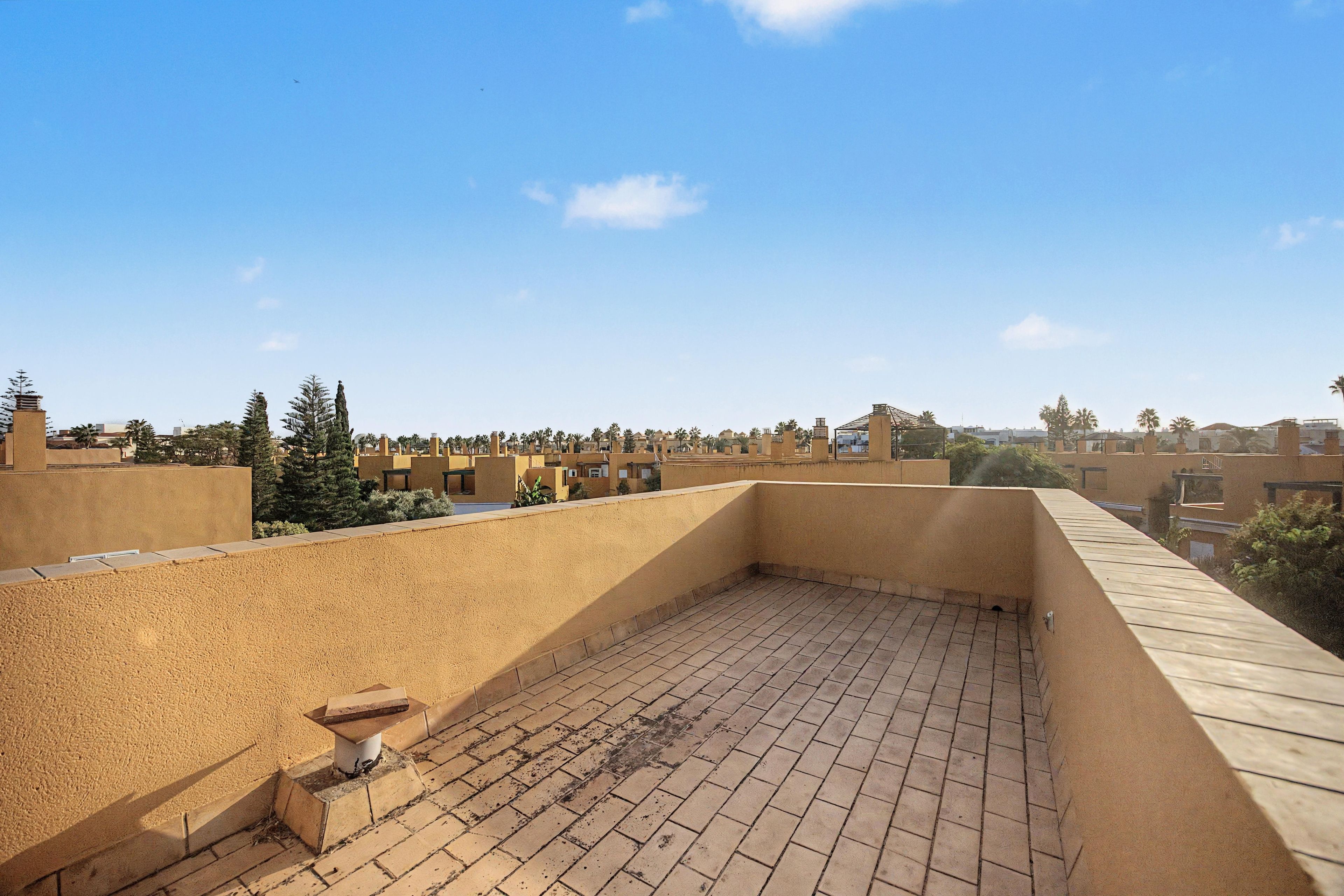 A rooftop terrace with a brick floor and a view of surrounding buildings.
