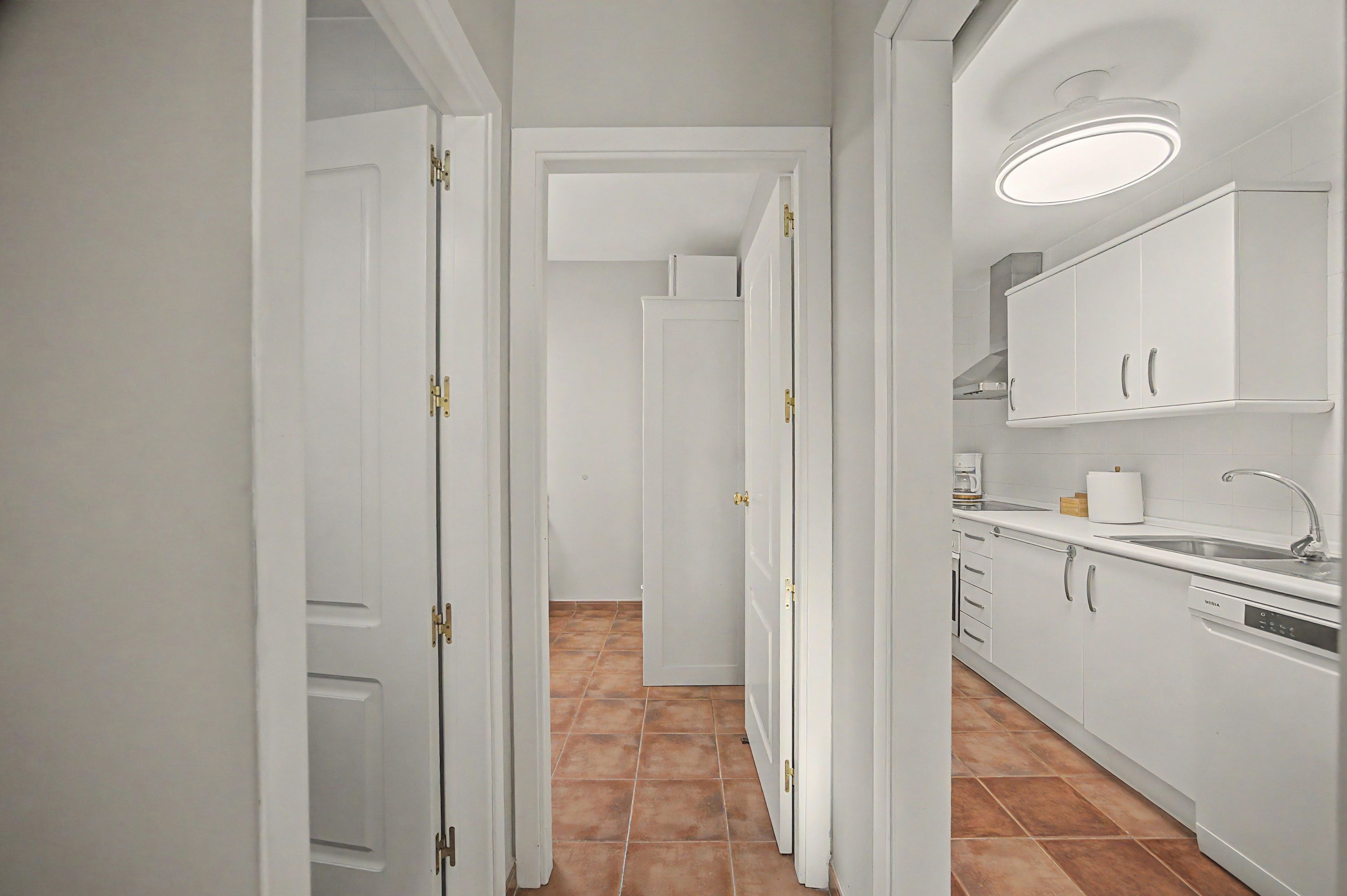 A narrow hallway leading to a kitchen with white cabinets and a built-in oven.