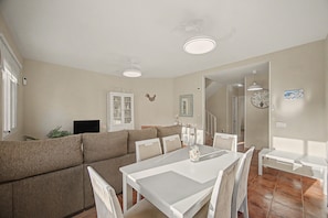 A dining area with a white table and chairs, a sofa, a cabinet with glass doors, and a wall-mounted clock. - Casa Tartessos with Pool and Parking in Costa Ballena (Rota)