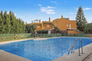 A swimming pool with a metal ladder, surrounded by a fence, and buildings in the background. - Casa Tartessos with Pool and Parking in Costa Ballena (Rota)
