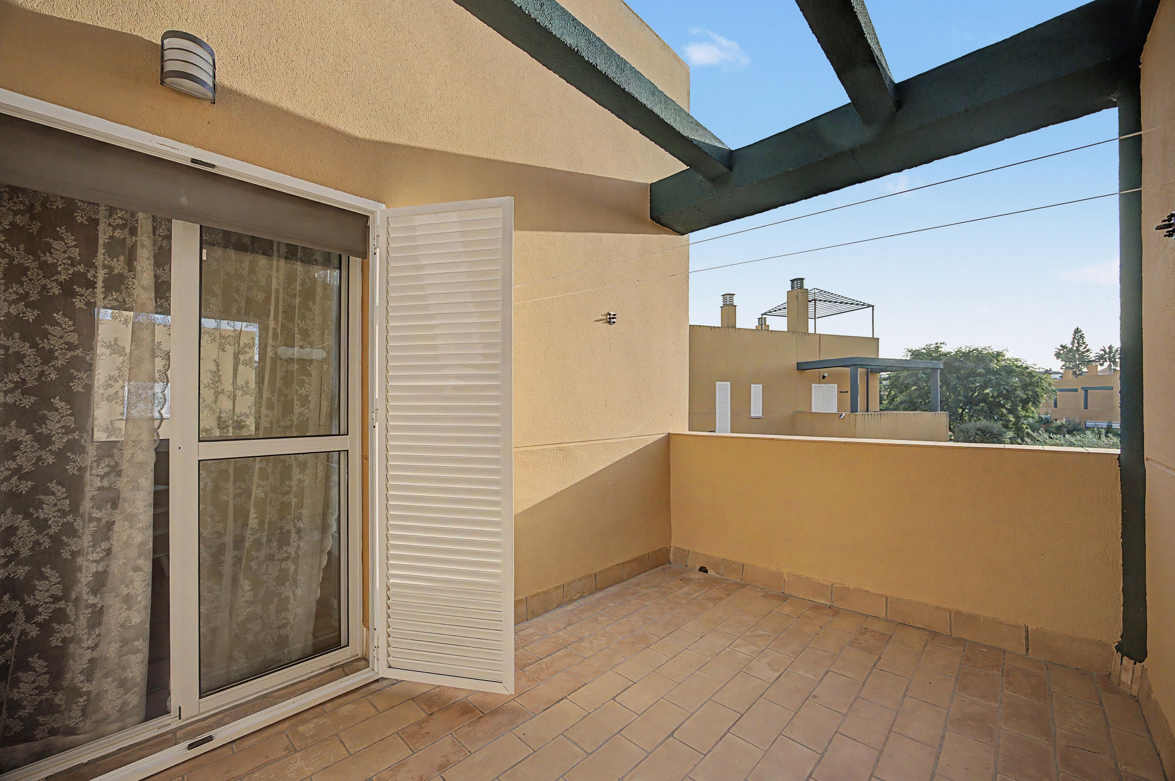 Un balcon doté d’une porte-fenêtre coulissante, d’un sol carrelé et offrant une vue sur les bâtiments voisins.
