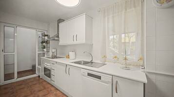 Een moderne keuken met witte kastjes, een inbouwoven, een vaatwasser en een raam met gordijnen.