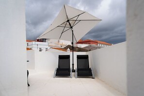 Terraço no telhado com um grande guarda-sol, duas portas pretas e uma parede branca.