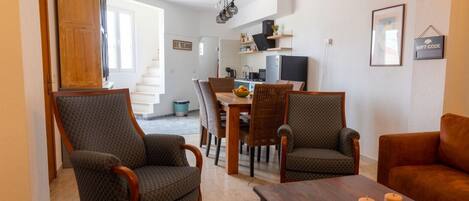 A modern living room with a dining area, featuring a wooden cabinet, wicker chairs, a brown leather sofa, and a wooden coffee table.