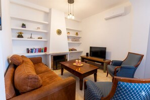 Ein Wohnzimmer mit einer Couch, Sesseln, einem Couchtisch, einem Kamin, einem Fernseher und Regalen mit Dekoration.