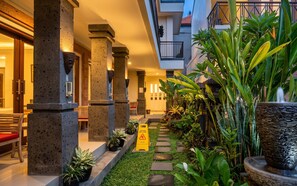 A hotel lobby with a wet floor sign, a staircase, and a variety of plants. - Rumah Kultur (Ubud)